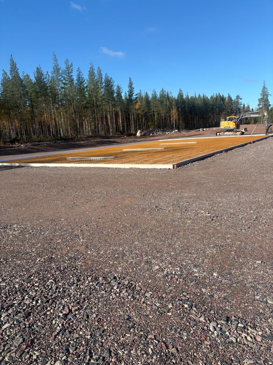 Formsatt och armerad grundbädd inför gjutning av betongplatta, med grävmaskin i bakgrunden