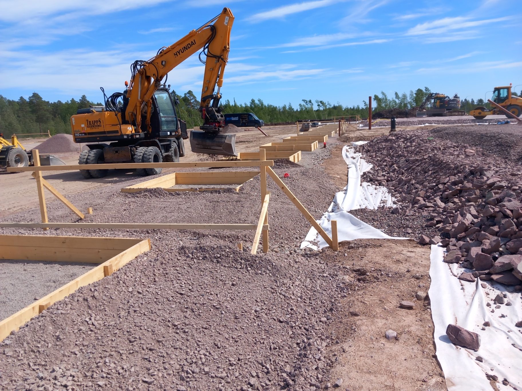 Gul Hyundai hjulgrävare med tiltrotator vid formsättning av grunder på en grusbädd